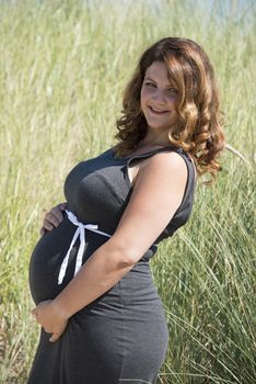 pregnant woman with white ribbon bow on her belly in nature with straw background