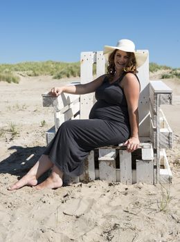 adult happy pregnant woman sitting on wooden chair on the beach