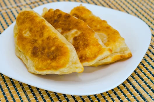 Three fried chebureks on the table on a white plate