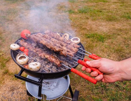 Closeup of a chef turning skewers of meat on hot barbecue