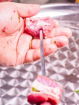 Closeup of a chef entering pieces of meat onto a skewer, making shish kebab