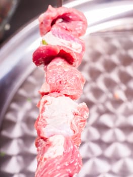 Closeup  of raw meat in sliceses entered on a skewer over metal plate