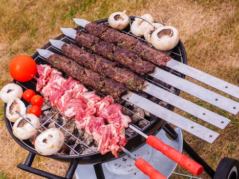 Shish kebab prepared over a black round shaped charcoal barbecue outdoors