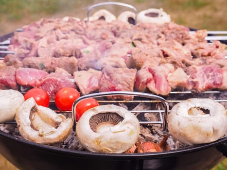 Shish kebab prepared over a black round shaped charcoal barbecue outdoors