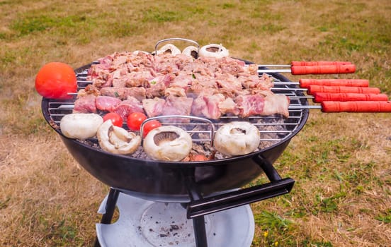 Shish kebab prepared over a black round shaped charcoal barbecue outdoors