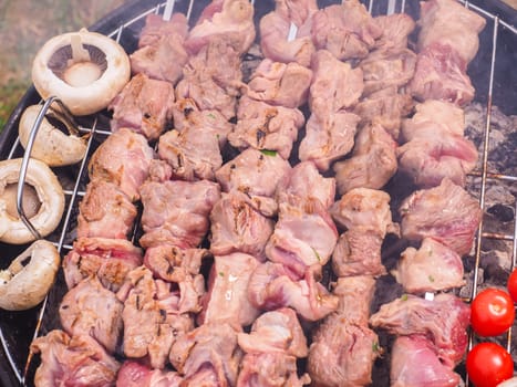 Shish kebab prepared over a black round shaped charcoal barbecue outdoors