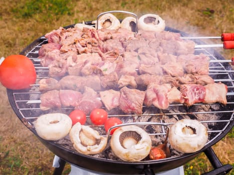 Shish kebab prepared over a black round shaped charcoal barbecue outdoors