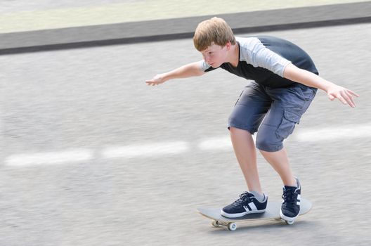 Young skater teenager guy in motion moving on skateboard along roadway against blurry asphalt background with copy-space area for text