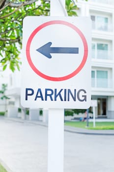 parking lot sign with left arrow and building in background