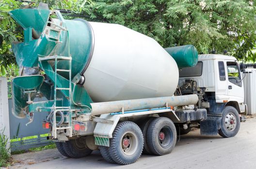 Concrete mixer truck with green cab over trees.