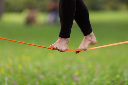 Lady practising slack line in the city park. Slacklining is a practice in balance that typically uses nylon or polyester webbing tensioned between two anchor points.