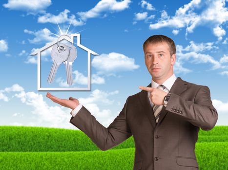 Business man hold house icon and metal keys in hand. Landscape as backdrop
