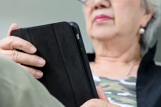 Senior women relaxing at home reading E-book on her tablet.