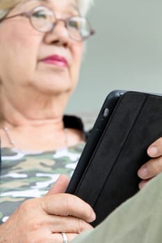 Senior women relaxing at home reading E-book on her tablet.