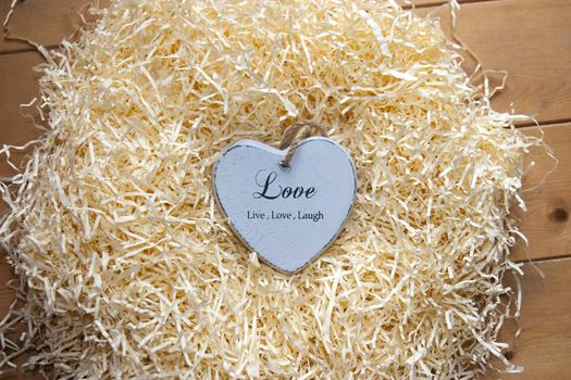 single grey wooden love heart in a love nest made of straw inscribed love, live and laugh