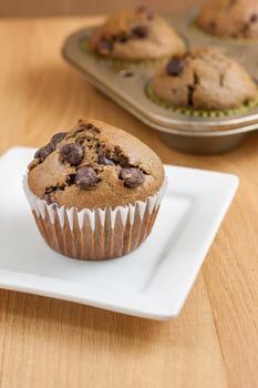 Chocolate chocolate chip muffins on a countertop with a pan of muffins in the back ground.