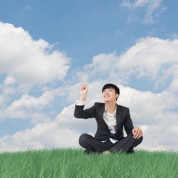 Businessman sit on grassland and finger toward the sky.