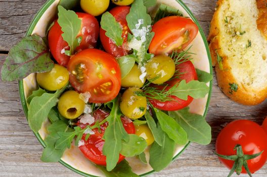 Fresh Tomatoes Salad with Arugula, Olives and Greens arranging with Garlic Bread closeup on Rustic Wooden background. Top View