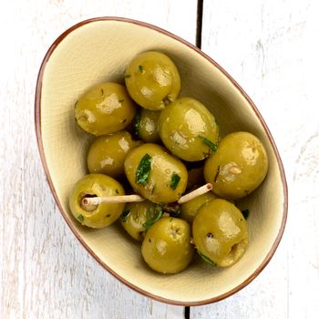 Tasty Appetizer with Green Olives, Olive Oil and Chopped Greens in Bowl on White Wooden background. Top View