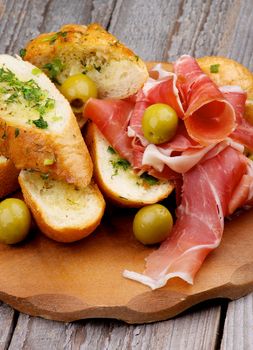 Delicious Tapas with Smoked Jamon, Garlic Bread and Green Olives on Wooden Plate closeup on Wooden background