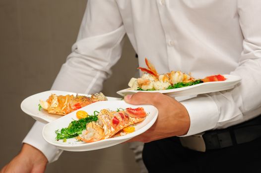 Waiter's hands holding plates with prepared lobster and sea weed
