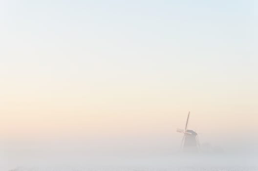 Windmill in the fog during a winter morning in a white landscape in Kinderdijk in Holland.