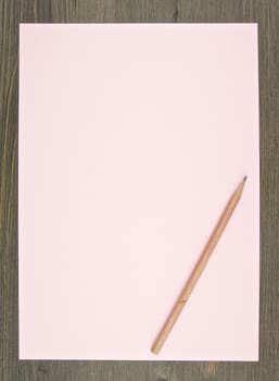 Brown pencil put on empty pink paper with wood background.