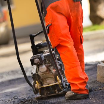 Construction workers during asphalting road works wearing coveralls. Manual labor on construction site.