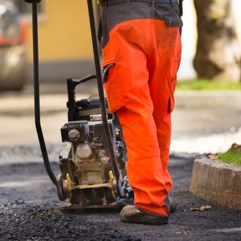 Construction workers during asphalting road works wearing coveralls. Manual labor on construction site.