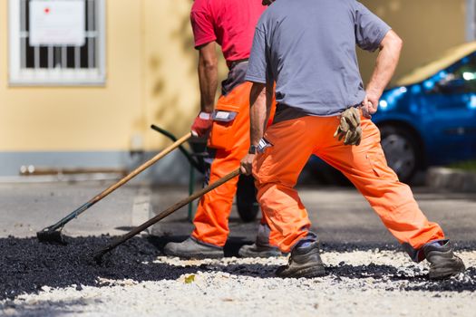 Construction workers during asphalting road works wearing coveralls. Manual labor on construction site.