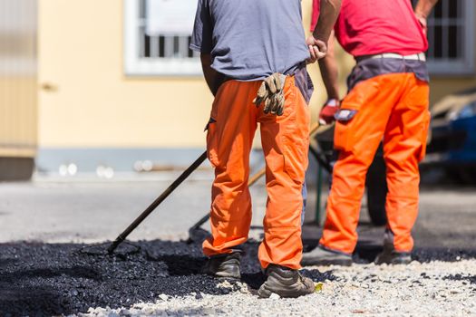 Construction workers during asphalting road works wearing coveralls. Manual labor on construction site.