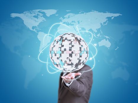 Business man hold exploding ball of gray puzzle pieces in hand. World map as backdrop