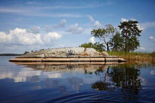 Island in the lake. Water landscape with stones. Stones in water. The lake with stones. Beautiful landscape. Water smooth surface and the blue sky with clouds.