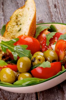 Tasty Tomatoes Salad with Arugula, Olives, Greens  and Garlic Bread in Bowl closeup on Rustic Wooden background
