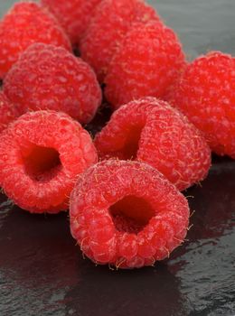 Heap of Fresh Sweet Raspberries with Water Drops on Black Wet background closeup. Vertical View