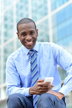 Smiling businessman sitting outdoors with cellphone