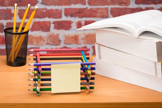 Desk with school supplies and colored pencil in front of brick wall 