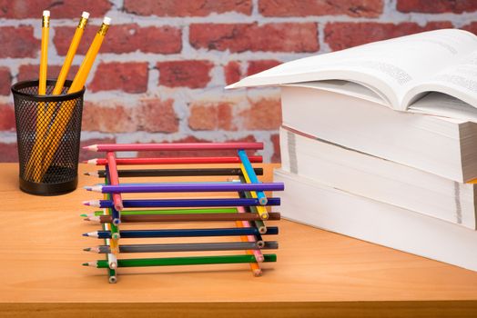 Desk with school supplies and colored pencil in front of brick wall 