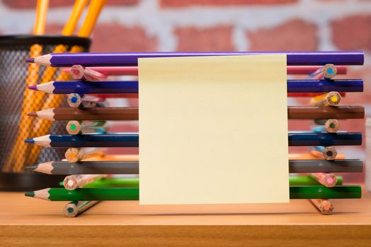 Desk with school supplies and colored pencil in front of brick wall 