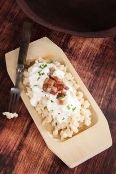 Bryndzove Halusky. Potato dumplings with bryndza sheep cheese and bacon on wooden plate on wooden background, top view. National traditonal slovak food. 