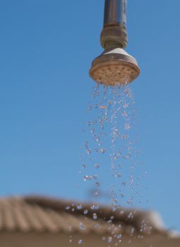 Outdoor shower head, against a deep blue summer sky, with water running from the shower head