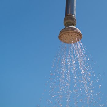 Outdoor shower head, against a deep blue summer sky, with water running from the shower head