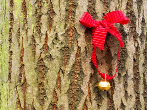 Photo shows detail of jingle bell with red ribbon in the wood