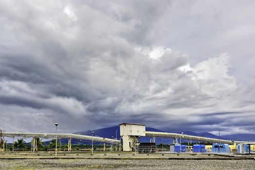 Coal power plant conveyor system shot against stormy clouds