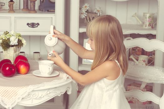 Little girl sitting at the table with fruits and teapot