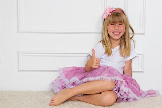 Little girl in a beautiful dress sits near a wall