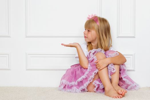 Little girl in a beautiful dress sits near a wall