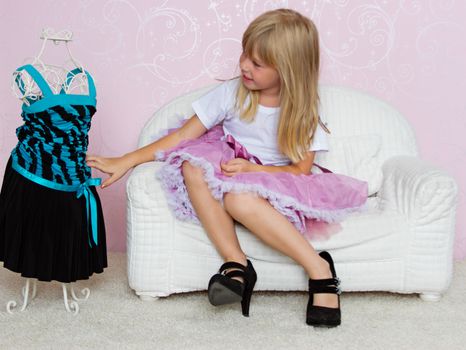 Girl in violet dress stands near mannequin in children store.