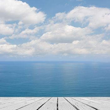 Empty wooden deck table with copyspace under sunny cloudy sky in the beach, focus on the wooden ground.