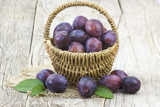 fresh plums in a basket on old wooden background